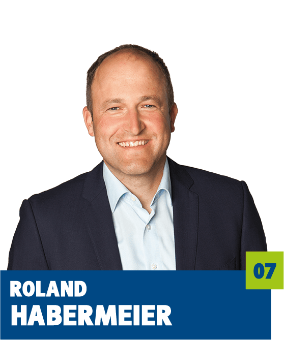 Professionelles Porträt von Roland Habermeier vor dunklem Hintergrund. Er trägt ein hellblaues Hemd und ein dunkles Sakko und lächelt offen in die Kamera. Der freundliche Gesichtsausdruck und der direkte Blick vermitteln Kompetenz, Seriosität und eine vertrauensvolle, nahbare Ausstrahlung und eignen sich sehr gut für die persönliche Vorstellung im beruflichen oder organisatorischen Kontext.