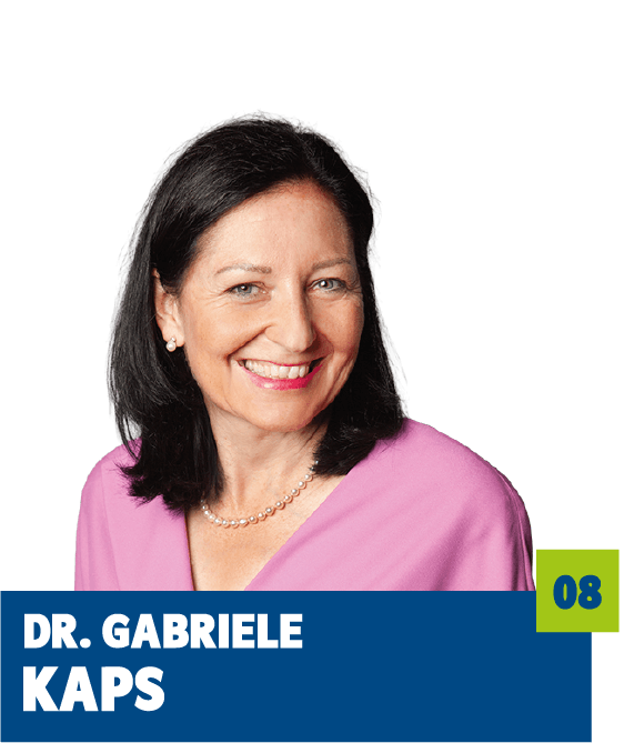 Professionelles Porträt von Dr. Gabriele Kaps vor dunklem Hintergrund. Sie trägt ein rosafarbenes Oberteil, eine Perlenkette und lächelt freundlich in die Kamera. Der offene Blick und die warme Farbwahl vermitteln Kompetenz, Vertrauen und eine sympathische, souveräne Ausstrahlung und eignen sich sehr gut für die persönliche Vorstellung im beruflichen, politischen oder organisatorischen Kontext.