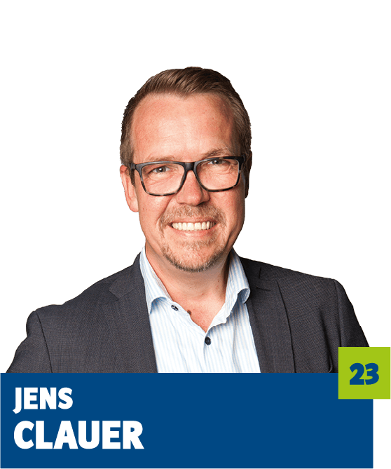 Professionelles Porträt von Jens Clauer vor dunklem Hintergrund. Er trägt ein helles Hemd, ein dunkles Sakko und eine Brille und lächelt freundlich in die Kamera. Der direkte Blick und das gepflegte Erscheinungsbild vermitteln Kompetenz, Offenheit und Seriosität und eignen sich sehr gut für die persönliche Vorstellung im beruflichen oder organisatorischen Kontext.