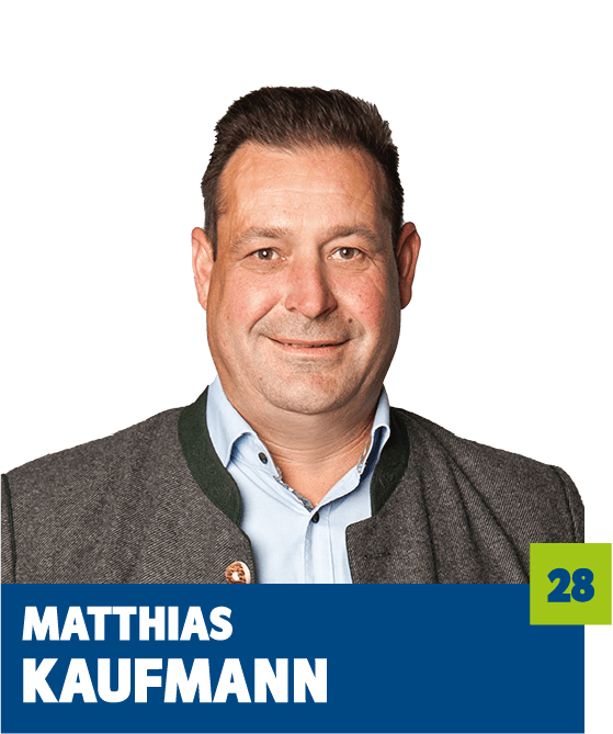 Professionelles Porträt von Matthias Kaufmann vor dunklem Hintergrund. Er trägt ein hellblaues Hemd und eine traditionelle graue Trachtenjacke mit grünem Kragen und Knopfdetail. Der direkte Blick in die Kamera vermittelt Bodenständigkeit, Seriosität und Vertrauen und eignet sich ideal für die persönliche Vorstellung im beruflichen oder organisatorischen Kontext.