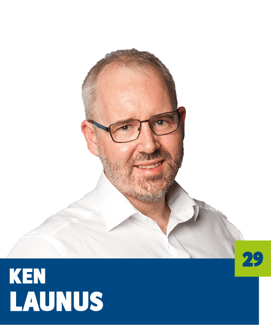 Professionelles Porträt von Ken Launus vor dunklem Hintergrund. Er trägt ein weißes Hemd und eine Brille und blickt freundlich in die Kamera. Das Bild vermittelt Kompetenz, Seriosität und eine persönliche Nahbarkeit und eignet sich sehr gut für die Vorstellung einer Person im beruflichen, unternehmerischen oder organisatorischen Umfeld.