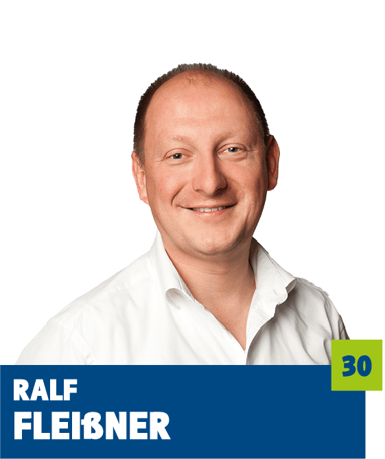 Freundliches Porträt von Ralf Fleißner vor dunklem Hintergrund. Er trägt ein weißes Hemd und lächelt offen in die Kamera. Das Bild vermittelt Seriosität, Offenheit und Vertrauen und eignet sich sehr gut für die persönliche Vorstellung einer Person im beruflichen, unternehmerischen oder organisatorischen Kontext.