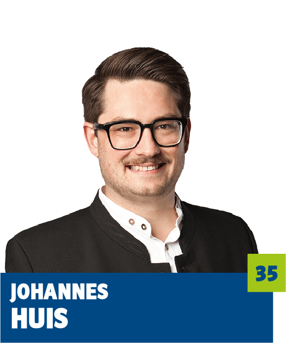 Freigestelltes Porträt eines Mannes vor dunklem Hintergrund. Er trägt eine schwarze Brille, ein weißes Hemd sowie ein dunkles Sakko und lächelt freundlich in die Kamera. Im unteren Bildbereich befindet sich ein grafisches Element mit dem Namen „Johannes Huis“ sowie einer hervorgehobenen Zahl. Das Porträt wirkt modern, sympathisch und professionell und eignet sich für politische, institutionelle oder redaktionelle Kommunikationsmedien.