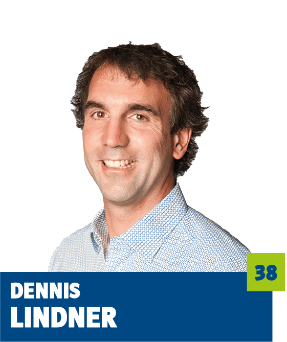 Freigestelltes Porträt eines Mannes vor dunklem Hintergrund. Er blickt freundlich lächelnd in die Kamera und trägt ein helles, gemustertes Hemd. Im unteren Bildbereich befindet sich ein grafisches Element mit dem Namen „Dennis Lindner“ sowie einer hervorgehobenen Zahl. Das Porträt wirkt offen, sympathisch und professionell und eignet sich für politische, institutionelle oder redaktionelle Kommunikationsmedien.