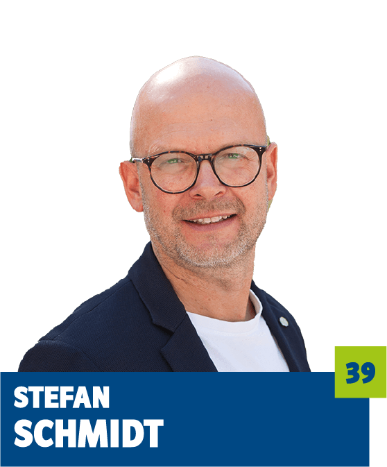 Freigestelltes Porträt eines Mannes vor dunklem Hintergrund. Er trägt eine Brille, ein dunkles Sakko und ein helles Shirt und blickt freundlich in die Kamera. Im unteren Bildbereich befindet sich ein grafisches Element mit dem Namen „Stefan Schmidt“ sowie einer hervorgehobenen Zahl. Das Porträt wirkt modern, offen und professionell und eignet sich für politische, institutionelle oder redaktionelle Kommunikationsmedien.