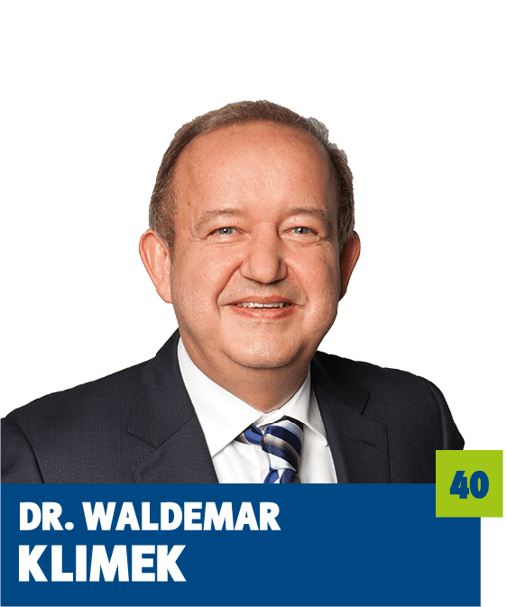 Freigestelltes Porträt eines Mannes vor dunklem Hintergrund. Er trägt einen dunklen Anzug, ein weißes Hemd und eine gestreifte Krawatte und blickt freundlich in die Kamera. Im unteren Bildbereich ist ein grafisches Textelement mit dem Namen „Dr. Waldemar Klimek“ sowie einer hervorgehobenen Zahl platziert. Die Aufnahme wirkt seriös und professionell und eignet sich für politische oder institutionelle Kommunikationsmedien.